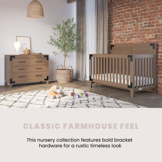 A cozy nursery with a rustic farmhouse vibe features the Child Craft Lucas 4-in-1 Convertible Crib in Dusty Heather, a matching dresser with black hardware, a woven lamp, basket plant, plush toy, and soft rug against a brick wall.
