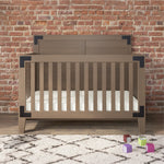 The Child Craft Lucas 4-in-1 Convertible Crib in Dusty Heather, featuring black metal corner accents, stands on a patterned rug before a brick wall, with four colorful toy blocks scattered nearby.
