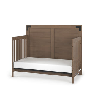 The Child Craft Lucas 4-in-1 Convertible Crib in Dusty Heather features a medium brown finish, high back panel, open slatted sides, black corner accents on the headboard, and comes with a white mattress.