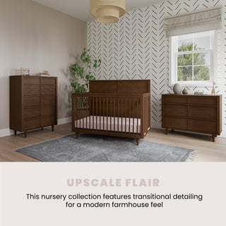 A modern nursery featuring the Child Craft Surrey Hill 3 Drawer Dresser in Toasted Chestnut, paired with dark wood furniture and set on a gray rug. Chevron accent wall, large window, and neutral walls complete the modern farmhouse style.