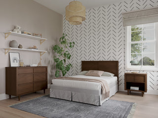 Modern bedroom with a bed, Child Craft Surrey Hill Nightstand in Toasted Chestnut, and a dresser. White chevron-patterned walls, potted plant, shelves with decor, woven ceiling lamp, large window, and gray rug on light wood floor.