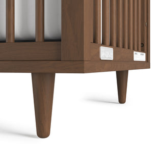 Close-up of the Surrey Hill 4-in-1 Convertible Crib by Child Craft in Toasted Chestnut, showing the bottom corner with vertical slats, angled legs, and two labels on the lower rail, set against a white background.
