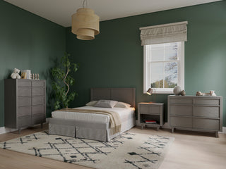 Modern bedroom with sage green walls, a double bed with gray linens, a matching nightstand, dresser, and the Surrey Hill 5 Drawer Chest by Child Craft in Lunar Gray, geometric rug, potted plant, basket pendant light, and a sunlit window.