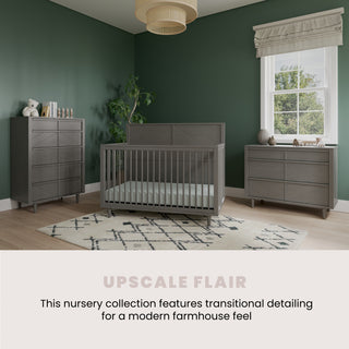 A modern nursery features the Child Craft Surrey Hill 4-in-1 Convertible Crib in Lunar Gray, paired with matching furniture against dark green walls, white-curtained windows, and a geometric rug for a modern farmhouse vibe.