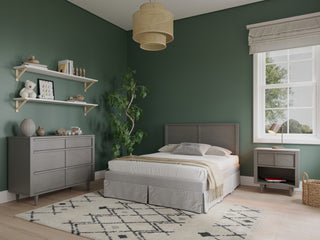 A cozy bedroom with green walls, a double bed, Child Craft Surrey Hill Nightstand in Lunar Gray, gray furniture, a patterned rug, potted plant, wall shelves with décor, a window with white curtains, and light wood flooring.