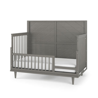 The Child Craft F09502 Toddler Guard Rail in Lunar Gray features a high back panel, low front rail, and side vertical slats. Pairs with Child Craft cribs for added safety and style. Includes a white mattress for a modern touch.