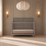 A Lunar Gray Child Craft Surrey Hill 4-in-1 Convertible Crib with a slatted design and a pink mattress, centered against a paneled wall in a nursery.
