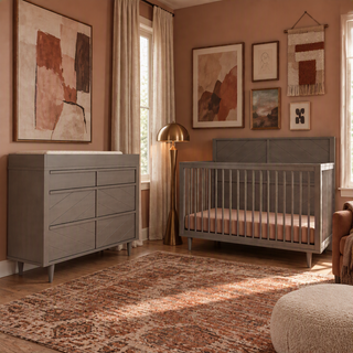 A gray Surrey Hill 4-in-1 Convertible Crib and matching six-drawer dresser in a nursery with an abstract rug, wall art, and a gold floor lamp.