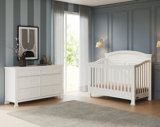 A modern nursery with the Child Craft Westgate 4-in-1 Convertible Crib in Vintage Linen, matching dresser, neutral rug, striped blue and paneled accent walls, a large window with sheer curtains, and wall art above the dresser.