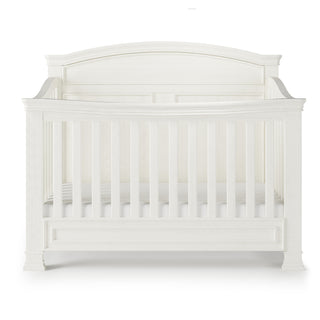 The Child Craft Westgate 4-in-1 Convertible Crib in Vintage Linen is shown from the front against a plain white background, crafted from pine with vertical slats, an arched headboard, decorative molding, and adjustable mattress support.