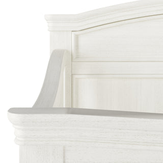 Close-up of the upper corner of the Child Craft Westgate 4-in-1 Convertible Crib in Vintage Linen, featuring a curved white wooden headboard with classic panel design and smooth, lightly textured finish—perfect for adjustable mattress support.