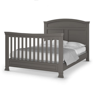The Child Craft F06424 Full-Size Bed Rails in Chelsea Gray add safety and versatility to your dark gray wooden bed with an arched headboard, a slatted footboard, and white and gray bedding.