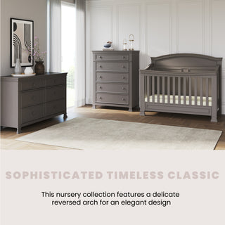 A bright, elegant nursery features Child Craft’s Westgate 4-in-1 Convertible Crib in Chelsea Grey, pine wood, with a tall dresser and wide dresser on a large light rug. Timeless design includes a delicate reversed arch for added style.