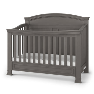 The Child Craft Westgate 4-in-1 Convertible Crib in Chelsea Grey features a high arched back, vertical slats on all sides, and decorative molding details, displayed against a white background.