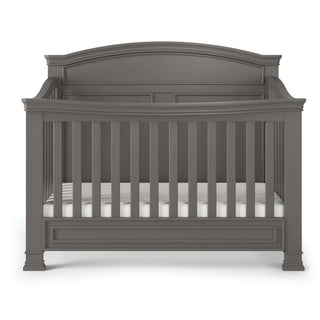 The Child Craft Westgate 4-in-1 Convertible Crib in Chelsea Grey features pine wood construction, vertical slats, an arched headboard, and decorative molding, displayed against a white background.