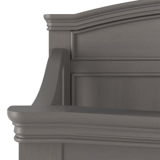 Close-up of the upper corner of the Child Craft Westgate 4-in-1 Convertible Crib in Chelsea Grey, highlighting its curved edges and detailed raised panel design on the headboard.