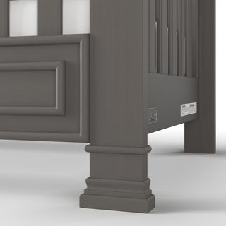 Close-up of the lower corner of the Child Craft Westgate 4-in-1 Convertible Crib in Chelsea Grey, featuring paneled detailing and sturdy legs, shown on a white background.