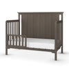 The Child Craft F09501 Toddler Guard Rail in Dapper Gray features sturdy wood construction, a high back panel, slatted sides, an open front with a partial guard rail, and supports a white mattress on its strong frame.