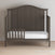 A Child Craft F09501 Toddler Guard Rail in Dapper Gray features strong wood construction, a partial safety rail, white mattress, and curved headboard, shown on a light wood floor against a plain light-colored wall.