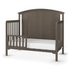 The Child Craft F09501 Toddler Guard Rail in Dapper Gray is a sturdy wooden bed with an arched headboard, vertical slats, and crib-style guard rail. Includes a white mattress and is shown against a white background.