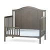 The Child Craft Toddler Guard Rail in Dapper Gray features sturdy wood construction with an arched headboard and vertical side slats, shown with a light blue patterned mattress.