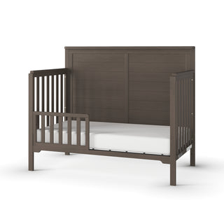 The Child Craft Toddler Guard Rail in Dapper Gray features sturdy wood construction, a high back panel, two side rails with vertical slats, and comes with a white mattress, all shown against a white background.