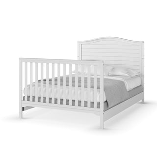 The Child Craft F06401 Full-Size Bed Rails in matte white, crafted from pine wood, add durability to a white wooden bed with slatted headboard and footboard, neatly dressed in white bedding and a light gray blanket against a plain background.
