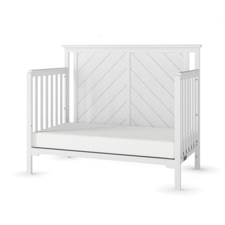 The Child Craft Hampton Flat Top 4-in-1 Convertible Crib in matte white features vertical side slats, a solid panel headboard with a diagonal line pattern, a plain white mattress, and is made from durable solid pine wood.