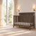 Child Craft Hampton Flat Top 4-in-1 Convertible Crib in Dapper Gray, featuring a flat top and chevron detail on the headboard, placed in a room next to a window.