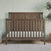 The Child Craft Hampton Flat Top 4-in-1 Convertible Crib in Dusty Heather with a chevron headboard sits on a light rug. A pale green wall with stars, potted plant, and wicker basket create a calm nursery ambiance.