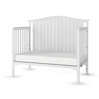 The Child Craft Hampton Arch Top 4-in-1 Convertible Crib in Matte White features a high, curved headboard, slatted sides, an open front, and adjustable mattress support—offering a simple, modern design ideal for any nursery.