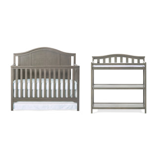 Front and back views of the Child Craft Hampton Arch Top 4-in-1 Convertible Crib in Dapper Grey, featuring a curved headboard, vertical slats, white mattress, adjustable mattress support, and sturdy horizontal support bars.