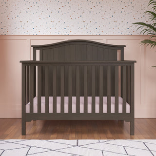 Hampton Arch Top 4-in-1 Convertible Crib in Dusty Heather, a dark gray crib with an arched top, vertical slats, and a light pink mattress.