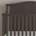 The Child Craft Hampton Arch Top 4-in-1 Convertible Crib in Dapper Grey features vertical slats, a curved headboard, and an adjustable mattress support with a white mattress, set against a light-colored wall.