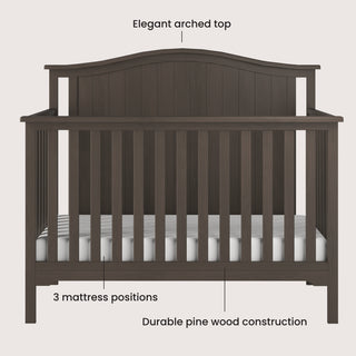 The Child Craft Hampton Arch Top 4-in-1 Convertible Crib in Dapper Grey features an elegant arched top, adjustable mattress support, and durable construction. Shown with a white mattress inside.