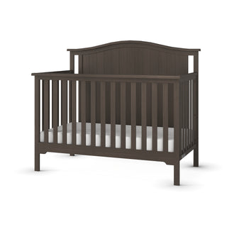 The Child Craft Hampton Arch Top 4-in-1 Convertible Crib in Dapper Grey features vertical slats, a high curved back panel, adjustable mattress support, and a white mattress, shown on a plain white background.
