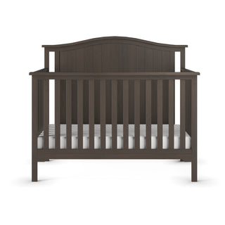 The Child Craft Hampton Arch Top 4-in-1 Convertible Crib in Dapper Grey features vertical slats, an arched headboard, and adjustable mattress support. Shown from the front with a white mattress on a plain white background.