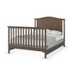 The Child Craft Hampton Arch Top 4-in-1 Convertible Crib in Dusty Heather features vertical slats on the headboard and footboard, shown with white bedding and a gray blanket, and photographed against a white background.
