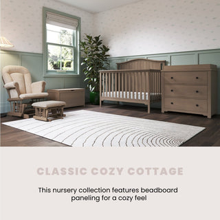 A cozy nursery with green beadboard, crib, dresser, toy chest, plant, and striped rug features the Child Craft Cozy Glider and Ottoman in Dusty Heather. Sunlight pours in as "CLASSIC COZY COTTAGE" describes the collection.