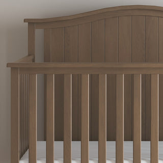 A close-up of the Child Craft Hampton Arch Top 4-in-1 Convertible Crib in Dusty Heather, featuring a high curved headboard, vertical slats, simple design, and a white mattress.