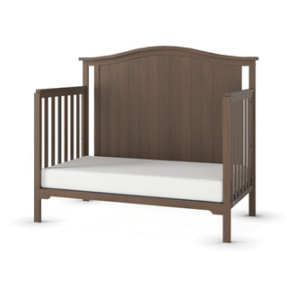 The Child Craft Hampton Arch Top 4-in-1 Convertible Crib in Dusty Heather features slatted sides, a high curved headboard, and a white mattress, displayed against a white background.
