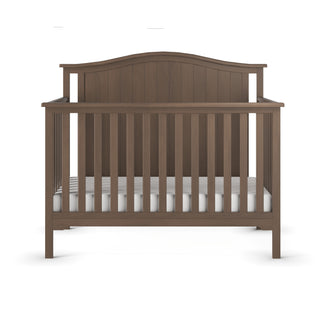 The Child Craft Hampton Arch Top 4-in-1 Convertible Crib in Dusty Heather features vertical slats, a curved headboard, a white mattress, and a simple classic design, shown from the front.