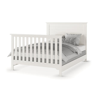 The Child Craft F06401 full-size bed rails in brushed cotton feature sturdy pine wood construction with a slatted white headboard and footboard, displayed with gray and white bedding and multiple pillows on a plain white background.