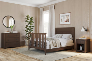 A cozy bedroom features a pine wood bed, nightstand, dresser, light walls, large plant, round mirror, framed art, and soft curtains over two windows. Neutral bedding and rug add warmth. Child Craft F06401 Full-Size Bed Rails in Brushed Truffle offer style and support.
