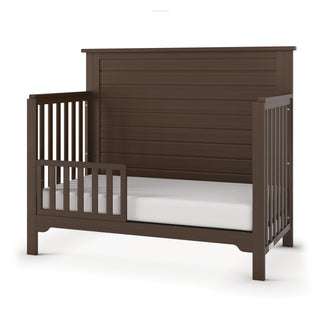 The Child Craft F09501 Toddler Guard Rail in Brushed Truffle features open side slats and a high paneled headboard. Designed for easy crib conversion, it comes with a low front rail and includes a white mattress.