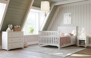 A cozy attic children's bedroom with slanted green walls, white furniture including a bed with Child Craft F06401 Full-Size Bed Rails in Brushed Cotton, dresser, nightstand, stuffed animals, a sunlit window, and soft neutral decor.