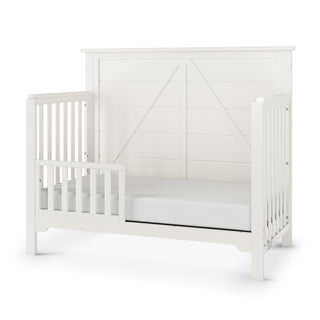The Child Craft F09501 Toddler Guard Rail in Brushed Cotton adds safety to your crib conversion, featuring a white wooden finish and modern farmhouse style—ideal for securing your toddler's bed.