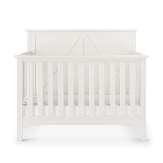 The Child Craft Woodland 4-in-1 Convertible Crib in Brushed Cotton features a modern white wooden design with vertical slats and a decorative solid back panel. The crib is empty, highlighting its clean style.