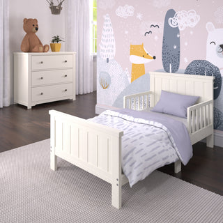 A cozy children’s bedroom with a white wooden bed, light purple bedding, the Child Craft Harmony 3-Drawer Dresser with Changing Table Topper in Brushed Cotton, playful animal wallpaper, and a gray rug on the dark wooden floor.