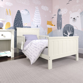 A child's bedroom with a white bed, lavender bedding, a Child Craft Harmony Nightstand in Brushed Cotton, and a light gray rug. The walls are decorated with whimsical pastel animal and tree illustrations.